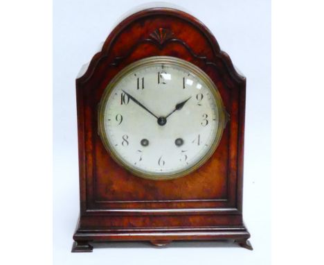 An early 20th century walnut cased mantel clock - the shaped arched case raised on bracket feet, the silvered dial set out in