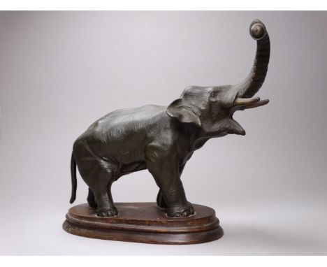 An early 20th century spelter model of an elephant - trunk raised, holding a breadfruit, on an associated wooden base, height