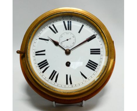 An early 20th century bulkhead timepiece - the circular brass case mounted on a mahogany disc, the white enamel dial set out 