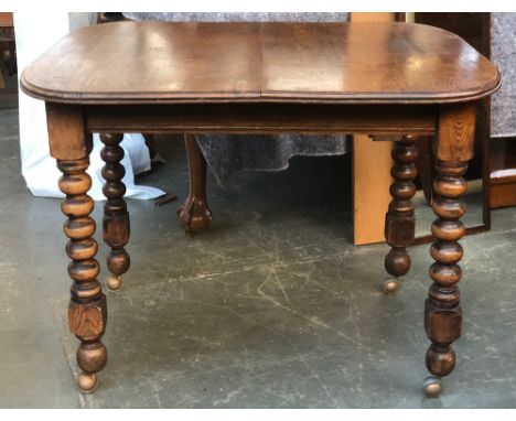 An early 20th century extending oak dining table, with spare leaf and winder, on bobbin turned legs and later casters, 74cmH 