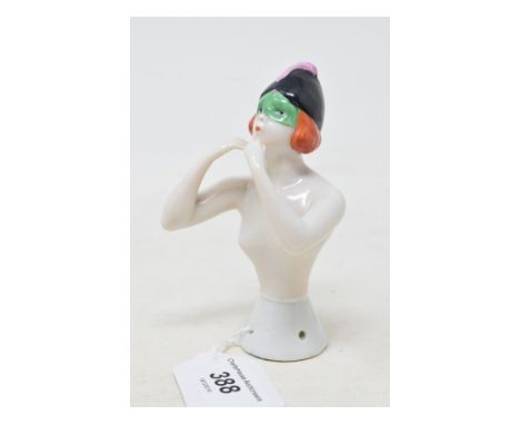 A porcelain half doll, probably Goebel, nude lady wearing a black cap and a green eye mask, blowing on fingers, impressed no.