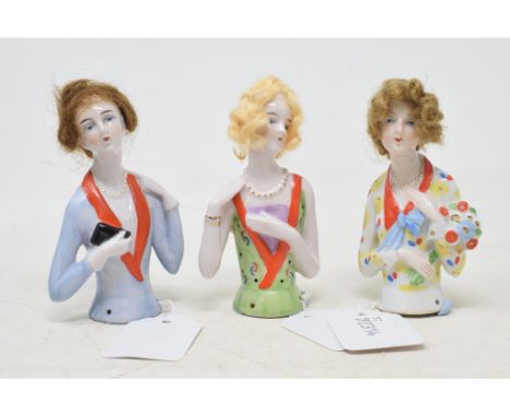 A porcelain half doll, lady wearing a light brown wig and a multi coloured dress, holding flowers, 10 cm high, and two others