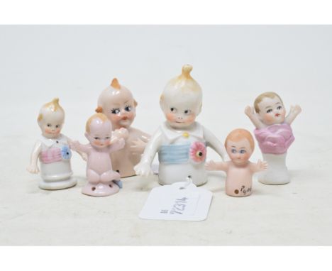 A Karl Schneider porcelain half doll, baby with a top knot, a white shirt and a blue sash, impressed mark to back, 7 cm high,