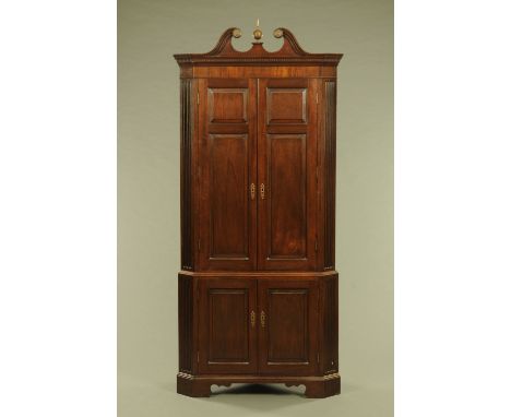 A George III style mahogany standing corner cupboard, with swans neck pediment above a pair of panelled doors opening to gree
