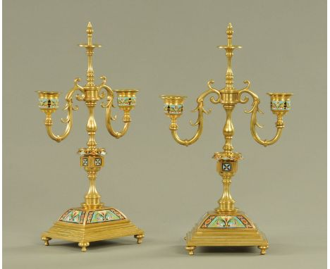 A pair of champleve enamel and brass two branch candelabra, each raised on a rectangular stepped base with four short feet.  