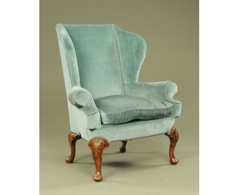 A Queen Anne style wing easy chair, with light blue upholstery and raised on shell carved cabriole legs terminating in pad fe