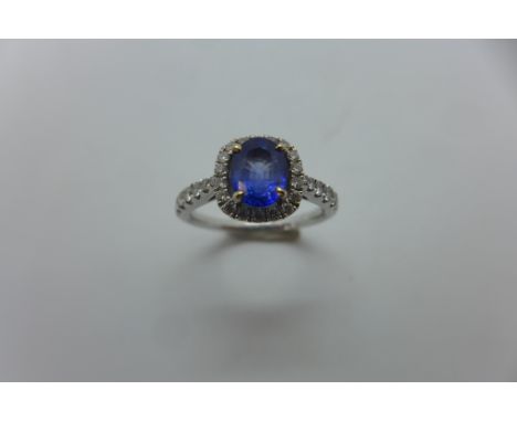 An 18ct white gold diamond and sapphire cluster ring, set in a mixed oval cut sapphire with halo border of round brilliant cu