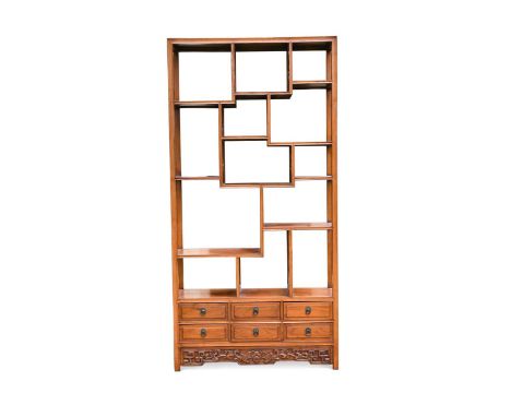 A Chinese elm open bookcase, 20th century, comprising various stepped compartments with pierced internal walls, over six draw