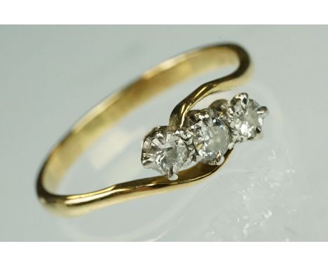 Diamond three stone yellow metal ring, three graduated small round cut diamonds, claw set, crossover shoulders, ring size O½ 