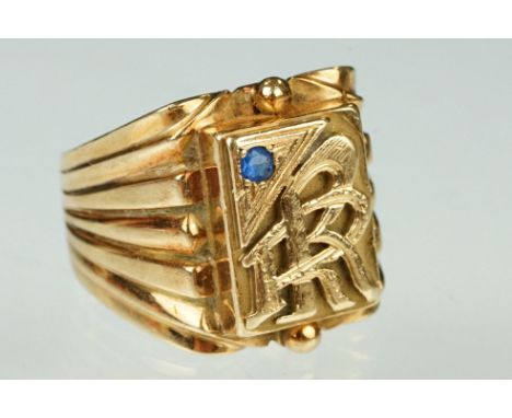 Yellow metal signet ring having a square head with interlaced R initials and a sapphire with reeded shoulders. Marked K14. Si