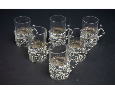 Six late Victorian tot glasses with silver glass holders, repoussé scene depicting putti collecting apples, the scroll handle