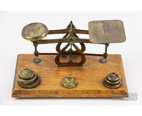 A set of small brass postage scales and seven weights, stamped J.W. &amp; Co., on oak base with bevelled edge, 20.5cm max.