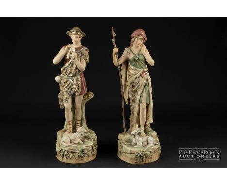 A pair of Royal Dux figures, of a shepherd playing pan-pipes, and a female goat herder with crabstock stave, pink pad marks, 