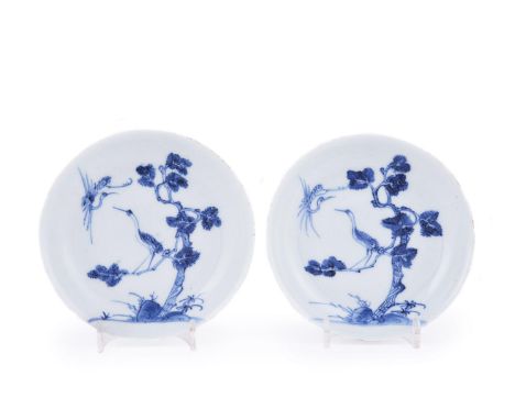 An unusual pair of Chinese blue and white saucers, Kangxi, painted with a crane perched in a pine tree with the companion cra