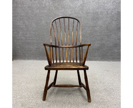 A 19th century elm stick back Windsor armchair having a high hooped back with outswept arms over a shaped patinated seat rais