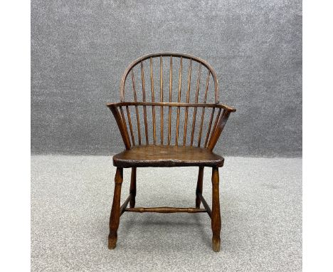 An early 19th century elm stick back Windsor armchair having a curved hoop back with outswept arms over a shaped and patinate
