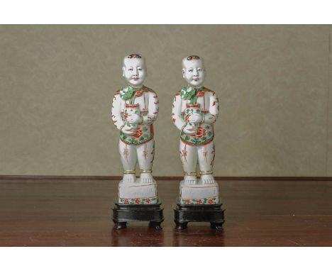 A PAIR OF FAMILLE VERTE MODELS OF BOYS In the Kangxi style, holding a vase of lotus, with stands and individual boxes 23cm hi