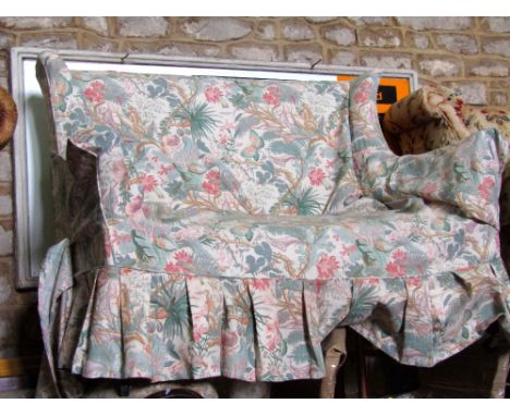An Edwardian/1920's two seat sofa with shallow shaped and winged back, simple linen upholstery and floral loose cover raised 