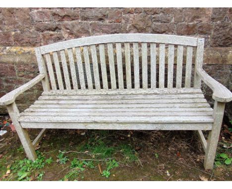 A weathered teak wood garden bench with stick back