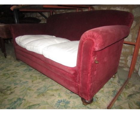 A late Victorian/Edwardian two to three seat sofa with rolled arms and single drop end, plum coloured upholstery and turned b