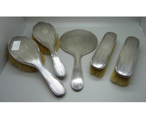 An Art Deco silver backed vanity set; four brushes and a hand mirror 
