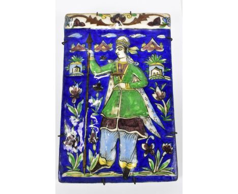 A 19th century Persian Qajar ceramic tile featuring a single figure holding a spear amongst floral detail on navy ground, 22.