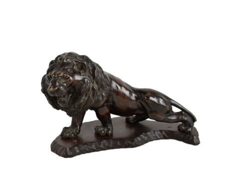 A large Japanese Meiji period bronze lion mounted on an adzed wooden base, signed to plaque to underside of belly, length 33.