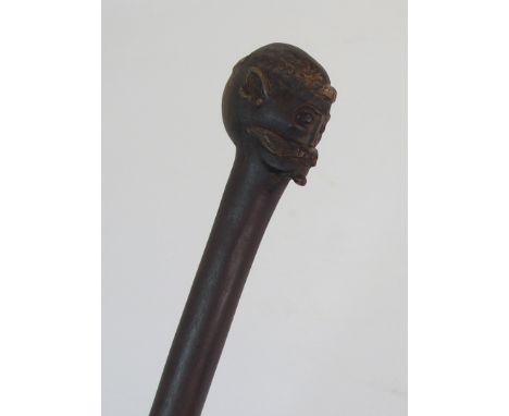 AN AFRICAN HARWOOD STICK the handle carved with a head and above a male figure running and holding  a shield, 105cm high Cond