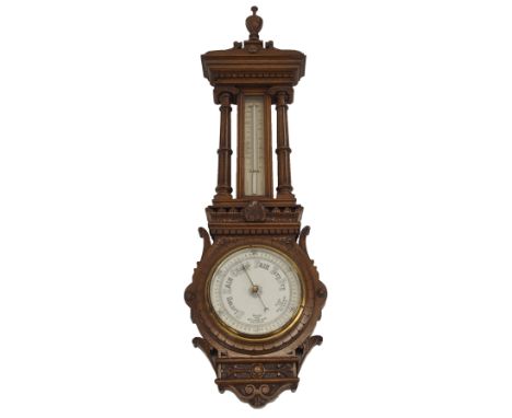 A VICTORIAN CARVED OAK ANEROID WHEEL BAROMETER/THERMOMETER with urn finial above fluted columns divided by anthemion leaf and