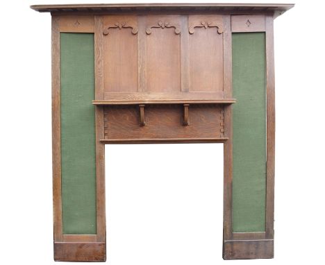 AN OAK ARTS AND CRAFTS FIRE SURROUND with over-hanging dentil cornice above scroll framed panels and inset baize panels with 