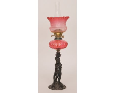 A late 19th Century oil lamp with a cast spelter base modelled as a putti before a large foliate scroll mounted with a compre
