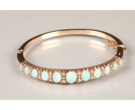 Gold stiff bangle set with eleven graduated oval opals, interspersed between small diamonds (28), largest opal 7.5mm long