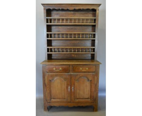 A French Oak Dresser, the boarded shelf back above two drawers and two arched cupboard doors, with a shaped apron flanked by 