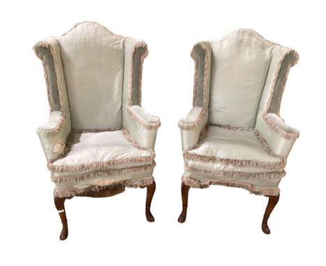 A pair of C18th upright high winged back armchairs, upholstered in a faded light green silk, on carved walnut cabriole legs t