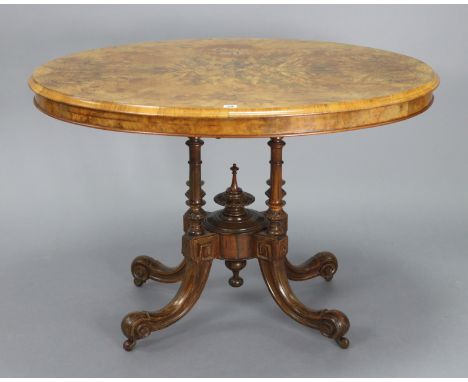 A Victorian burr-walnut oval tilt-top dining table on four turned &amp; fluted supports &amp; carved splay legs with ceramic 