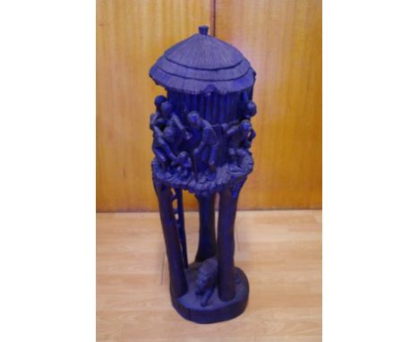Carved African tree trunk sculpture depicting figures surrounding an elevated hut with a lion  beneath, 87cm high approx