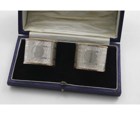 A GEORGE V CASED PAIR OF ENGINE-TURNED NAPKIN RINGS with applied, 9 ct. gold borders, one initialled "N", the other "M", by C