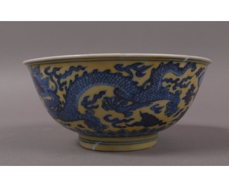 A CHINESE KANGXI MARK AND PERIOD YELLOW GROUND BOWL, finely decorated with dragons and clouds in underglaze-blue above a lapp