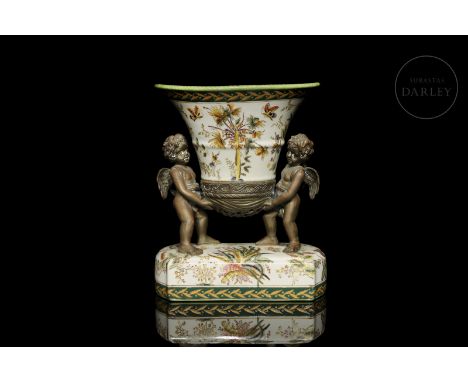 Glazed over-glazed ceramic base, with two small bronze angels holding a vessel. The floral and animal motifs stand out, as do