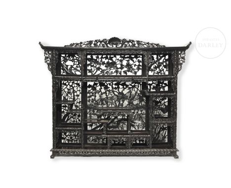 The carved wood forms a rectangular-shaped shelf with tiered divisions, decorated with carved and openwork vegetal motifs tha