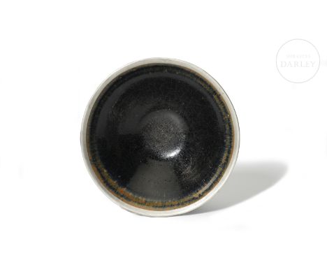 A bowl-shaped ceramic with a narrow circular base and a broad conical body. It is decorated with a thick two-tone glaze, in b