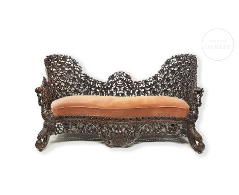 Carved wooden sofa with an elongated structure, curved back, wide legs and armrests. Decorated with openwork details of flowe