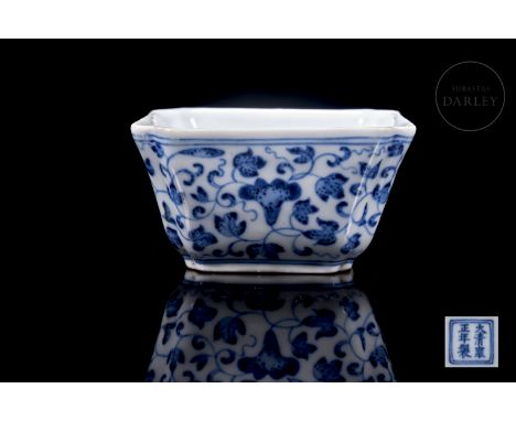 A small square vessel with lobed edges that expands slightly towards the mouth. On the outside, it is decorated with thin, cu