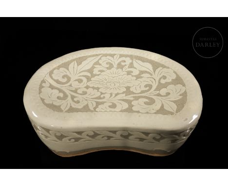 A traditional kidney-shaped, modelled ceramic pillow with a flat base and surface. It is decorated with sgraffito vegetal mot