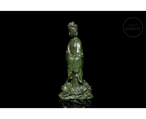 Green jade carved in the form of a beautiful Guanyin, standing above a raging sea from which large fish emerge. The deity sta