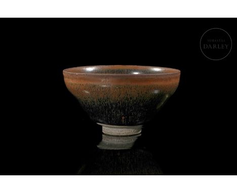 A ceramic vessel modelled and decorated with a thick two-tone black and brown glaze. It has a short circular foot on which re