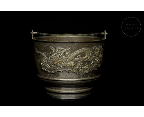 A bronze vessel with a large cylindrical body and a narrow foot, decorated with a relief image of a ferocious dragon with a c