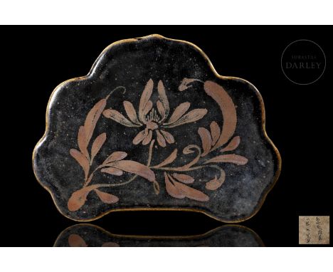 Ceramic modelled in the form of a pillow, with a lobed profile. It is decorated with a thick brownish-black iron-oxide glaze 