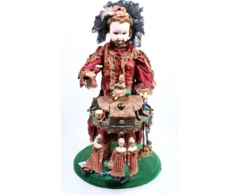 19th century bisque headed doll musical automaton dressed in Victorian costume standing by a table of toys, raised on plinth.