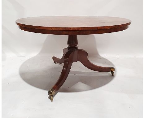 19th century snap-top circular table with figured top, turned column, on three ogee legs, brass caps and castors, 121cm diame